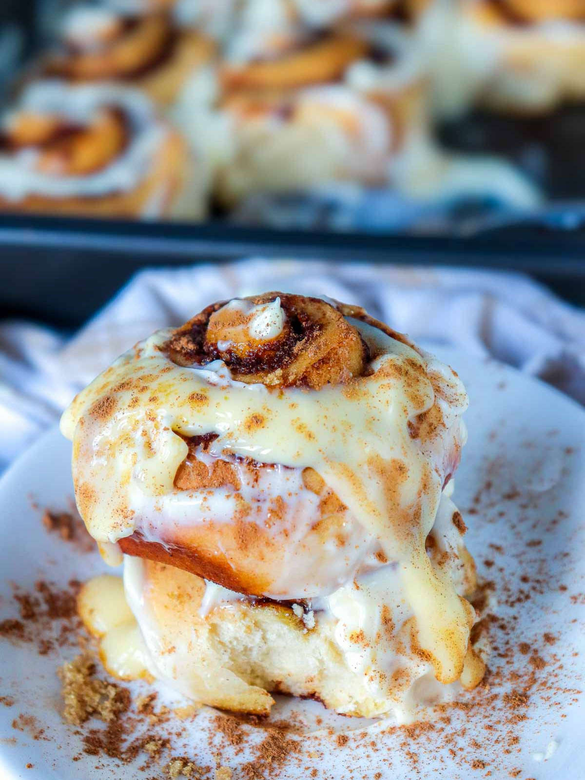 Two stacked pumpkin cinnamon rolls on a white plate, drizzled with maple cream cheese glaze and sprinkled with cinnamon.