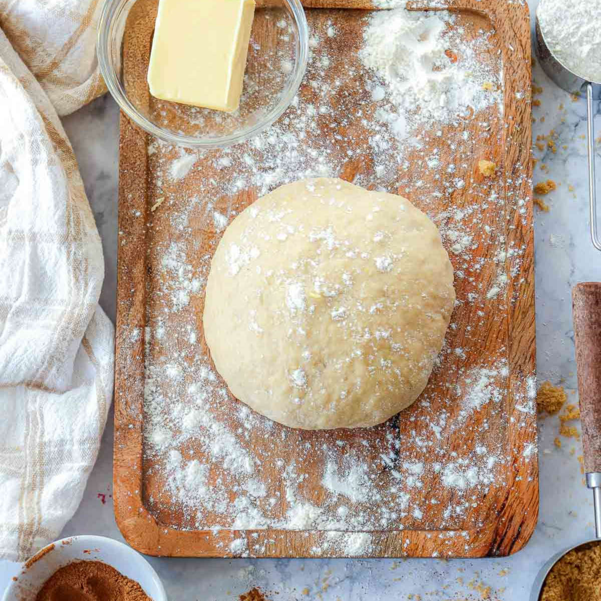 Ball of pumpkin-enriched dough resting on a floured wooden board, surrounded by butter and flour for kneading.
