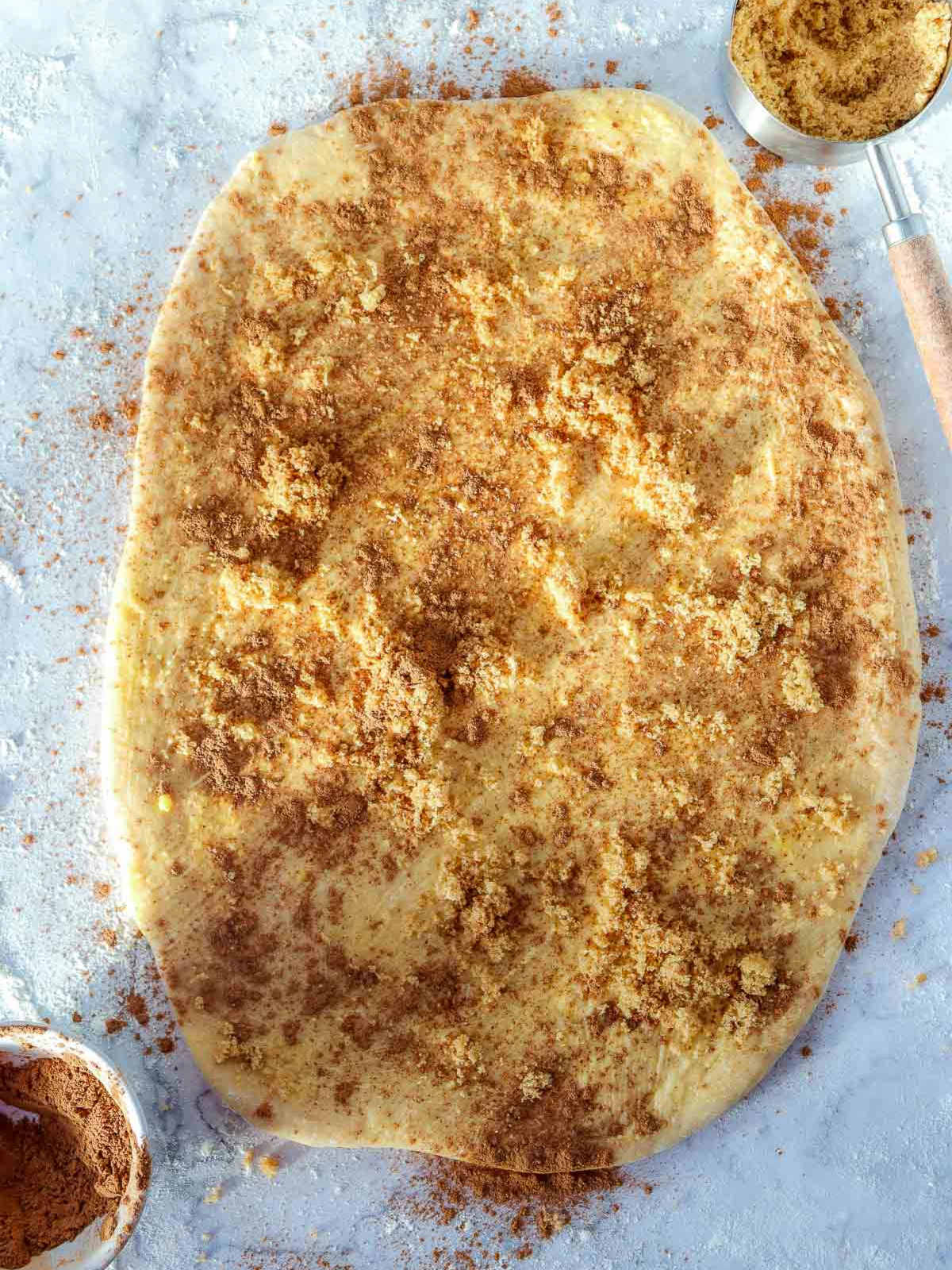 Rolled-out dough topped evenly with melted butter, brown sugar, cinnamon, and pumpkin spice filling.