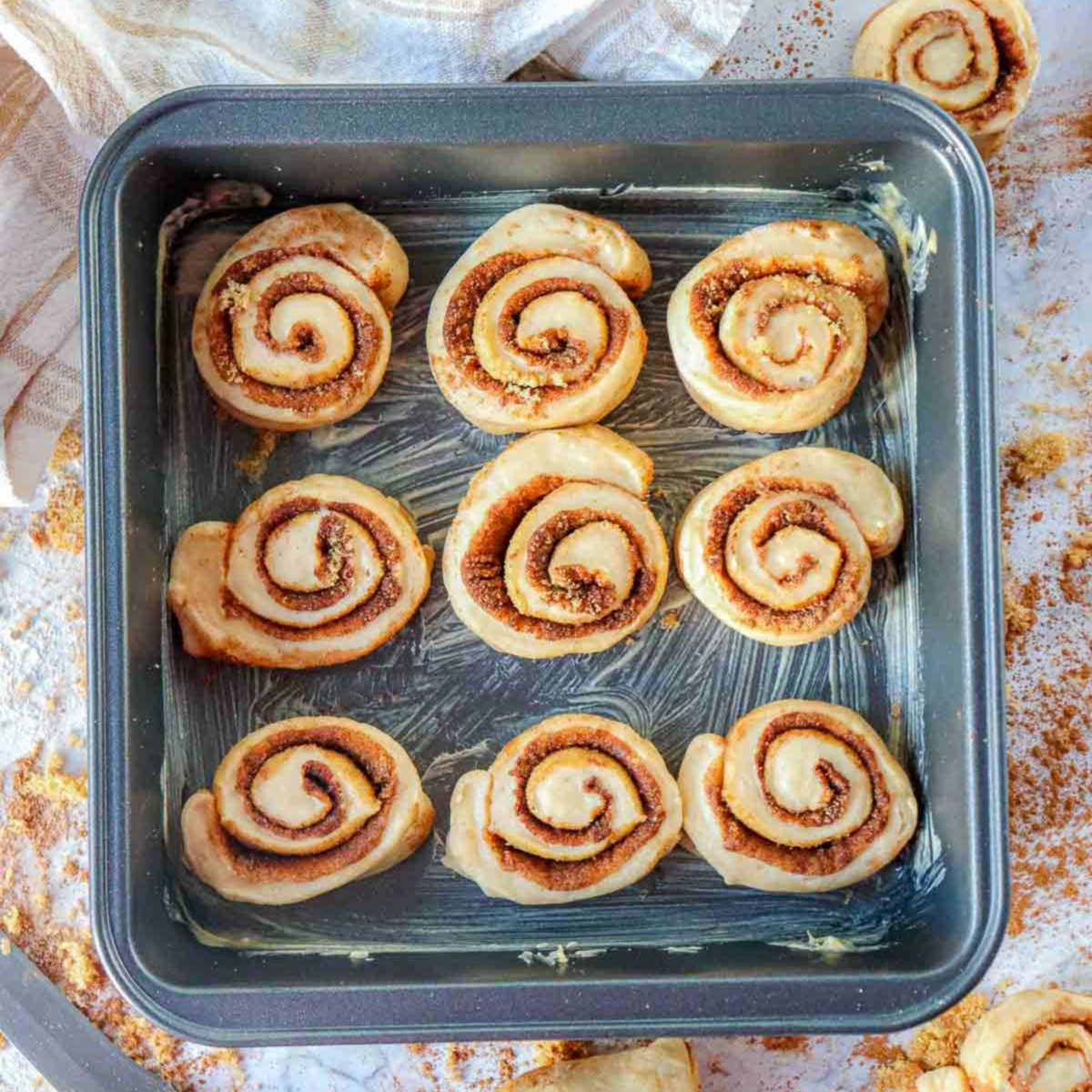 Unbaked pumpkin cinnamon rolls arranged in a greased square pan, ready for second rise before baking.