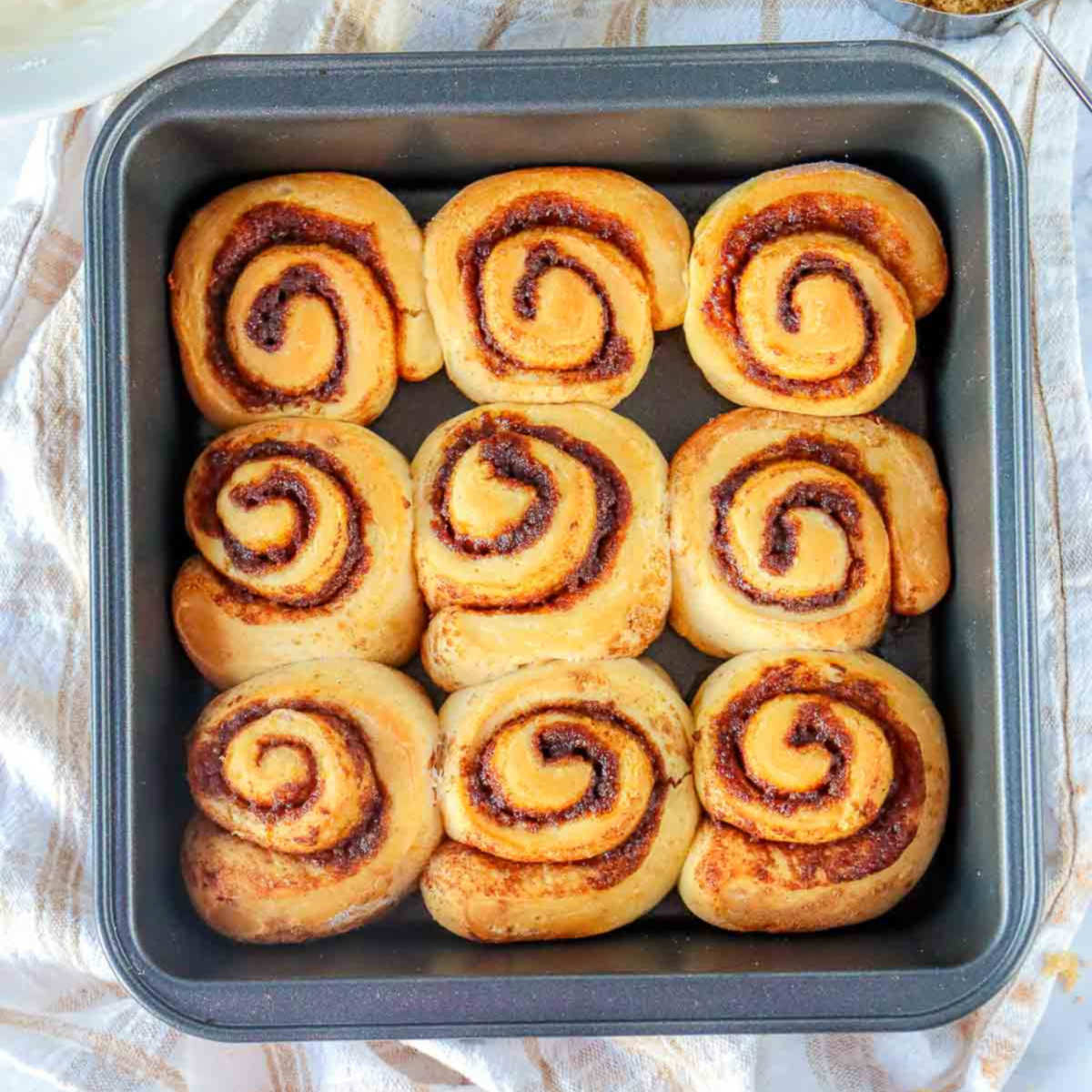 Freshly baked pumpkin cinnamon rolls in a square pan, golden brown with distinct spiral layers.