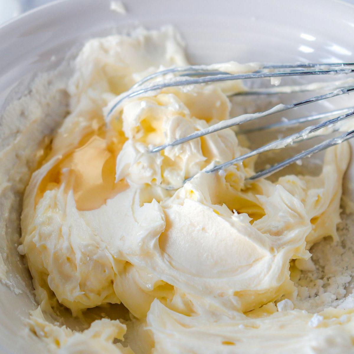 Maple cream cheese glaze being mixed in a bowl with a whisk, showing smooth creamy texture.