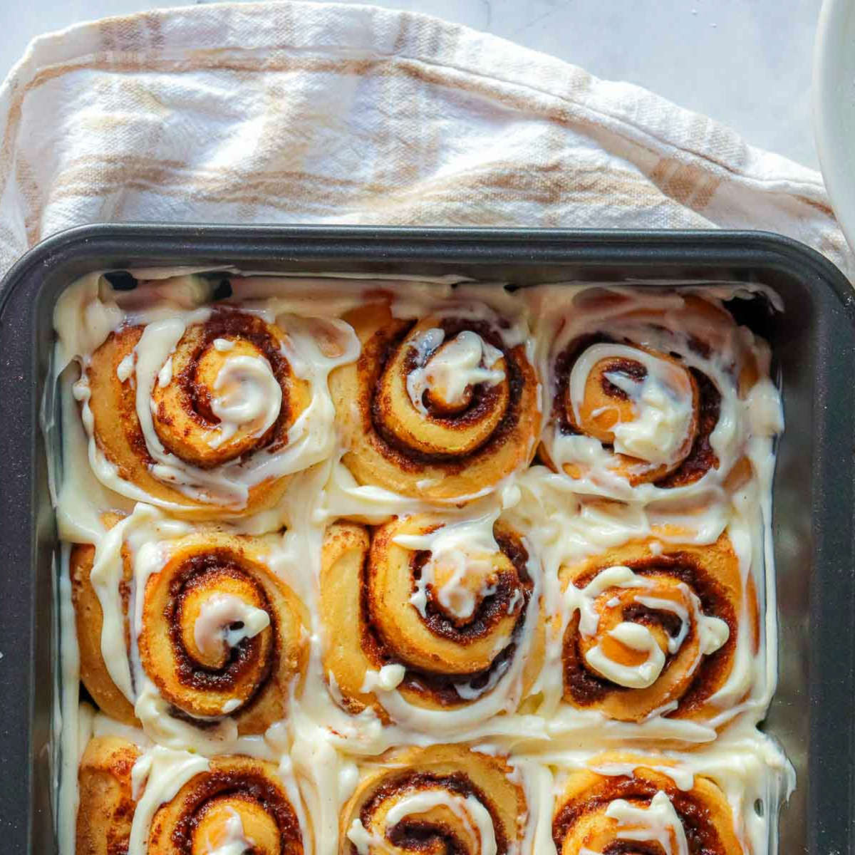 Baked pumpkin cinnamon rolls in pan generously topped with maple cream cheese glaze.