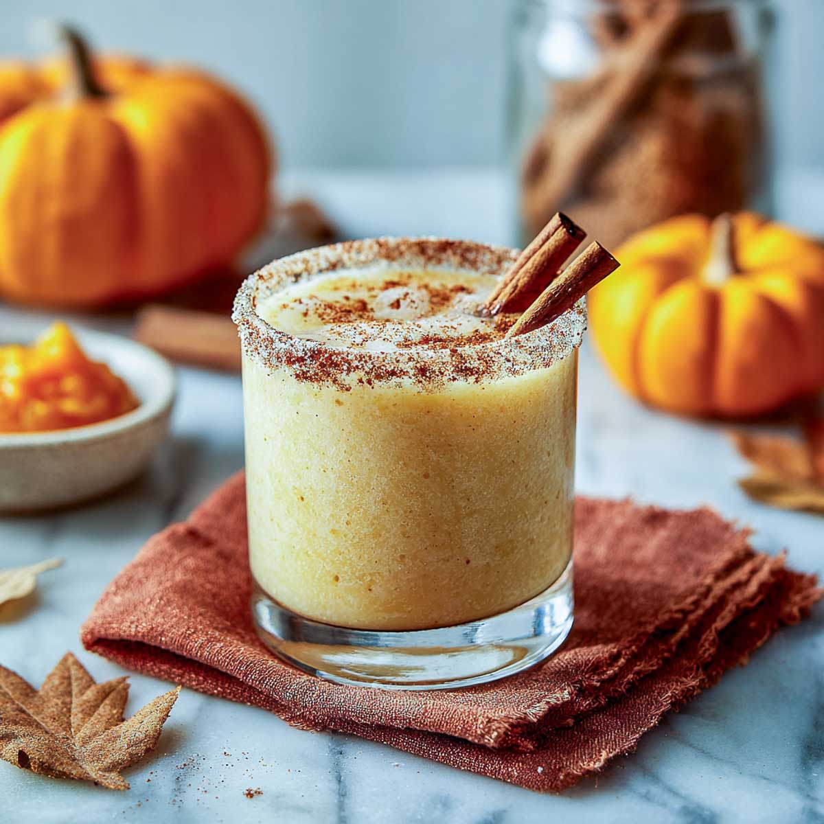 Pumpkin spice margarita with cinnamon rim and cinnamon sticks on marble surface.