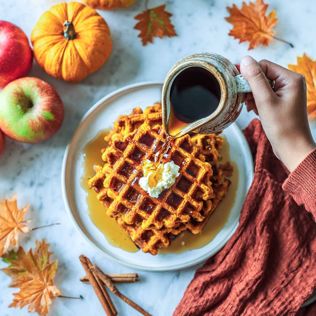 Overhead view of pumpkin waffles with syrup pour and whipped butter.