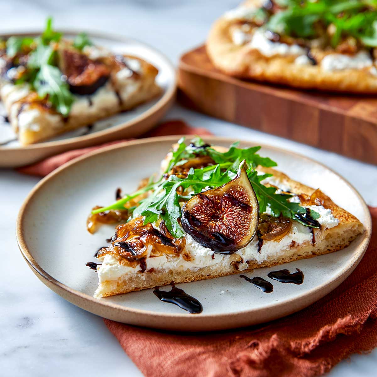 Slice of roasted fig flatbread with cottage cheese, arugula, and balsamic drizzle.