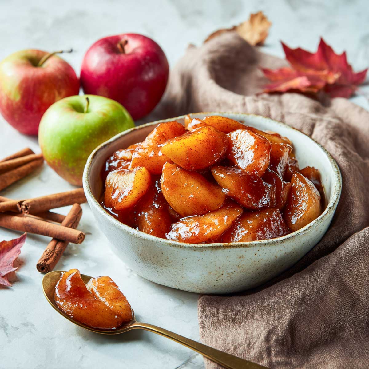 Side view of glossy cinnamon apples in bowl on marble surface.