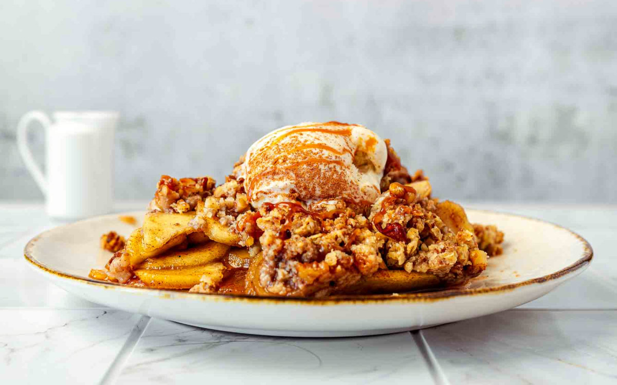 Close-up of apple crisp on a plate with vanilla ice cream and cinnamon caramel drizzle.