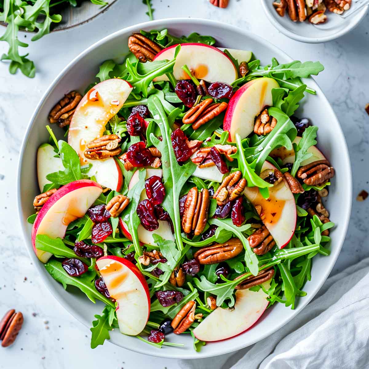 Apple pecan arugula salad with dried cranberries and cranberry vinaigrette in a white bowl.