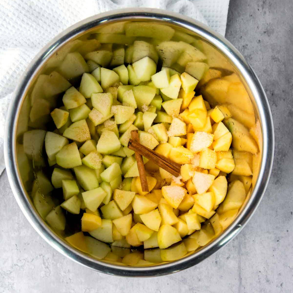Chopped apples with cinnamon sticks and sugar inside the Instant Pot before cooking.