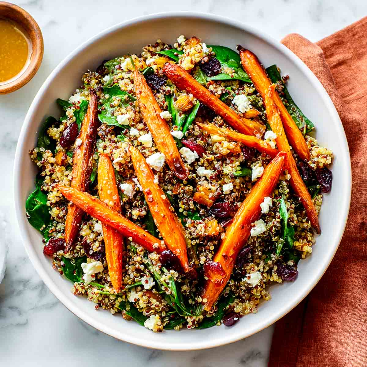 Autumn quinoa salad with maple-roasted carrots, spinach, cranberries, and vegan feta in a white bowl.