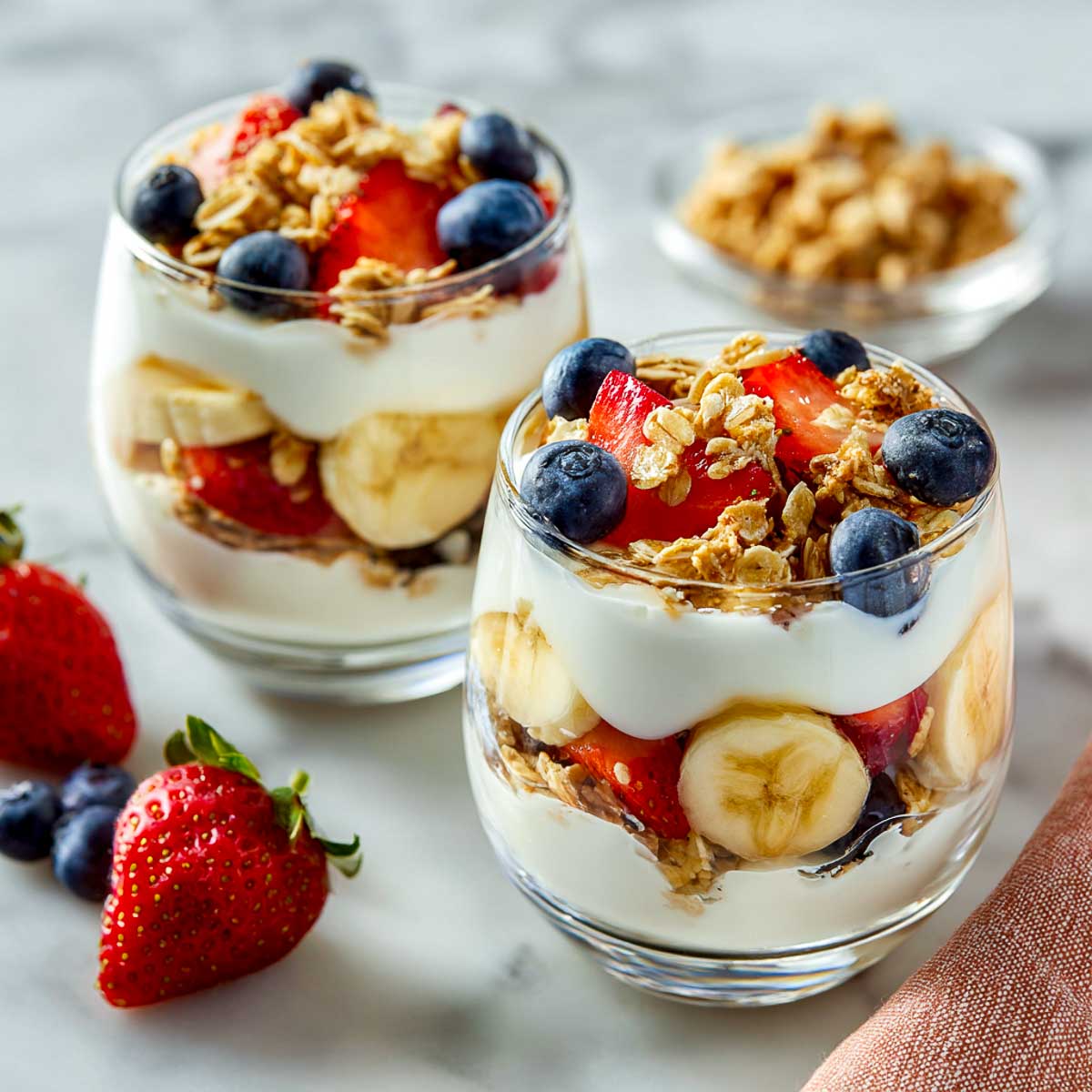 Yogurt parfaits with banana, berries, and granola in clear glass bowls.