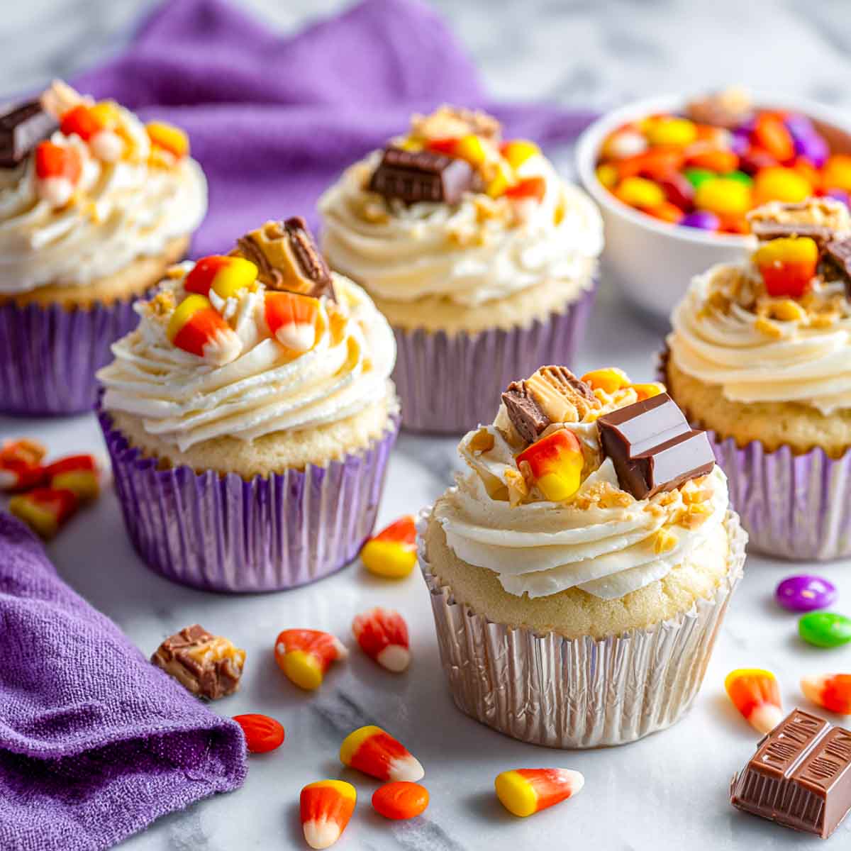 Cupcakes with white frosting topped with candy corn, chocolate bars, and crumbs.