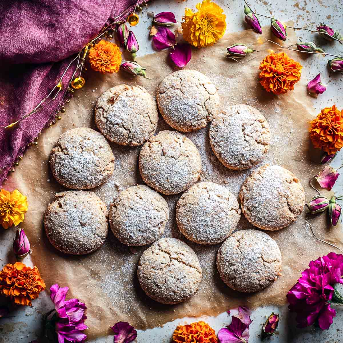 Batch of chai-spiced almond cookies dusted with sugar and surrounded by flowers.
