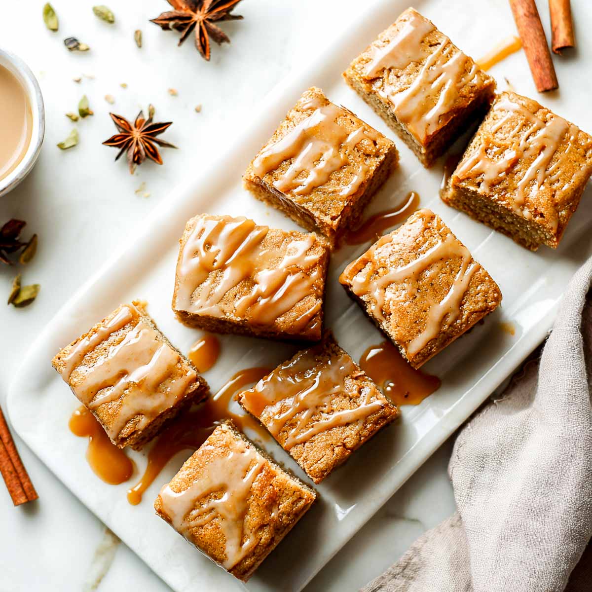 Chai-spiced vegan blondies drizzled with maple glaze on white platter.