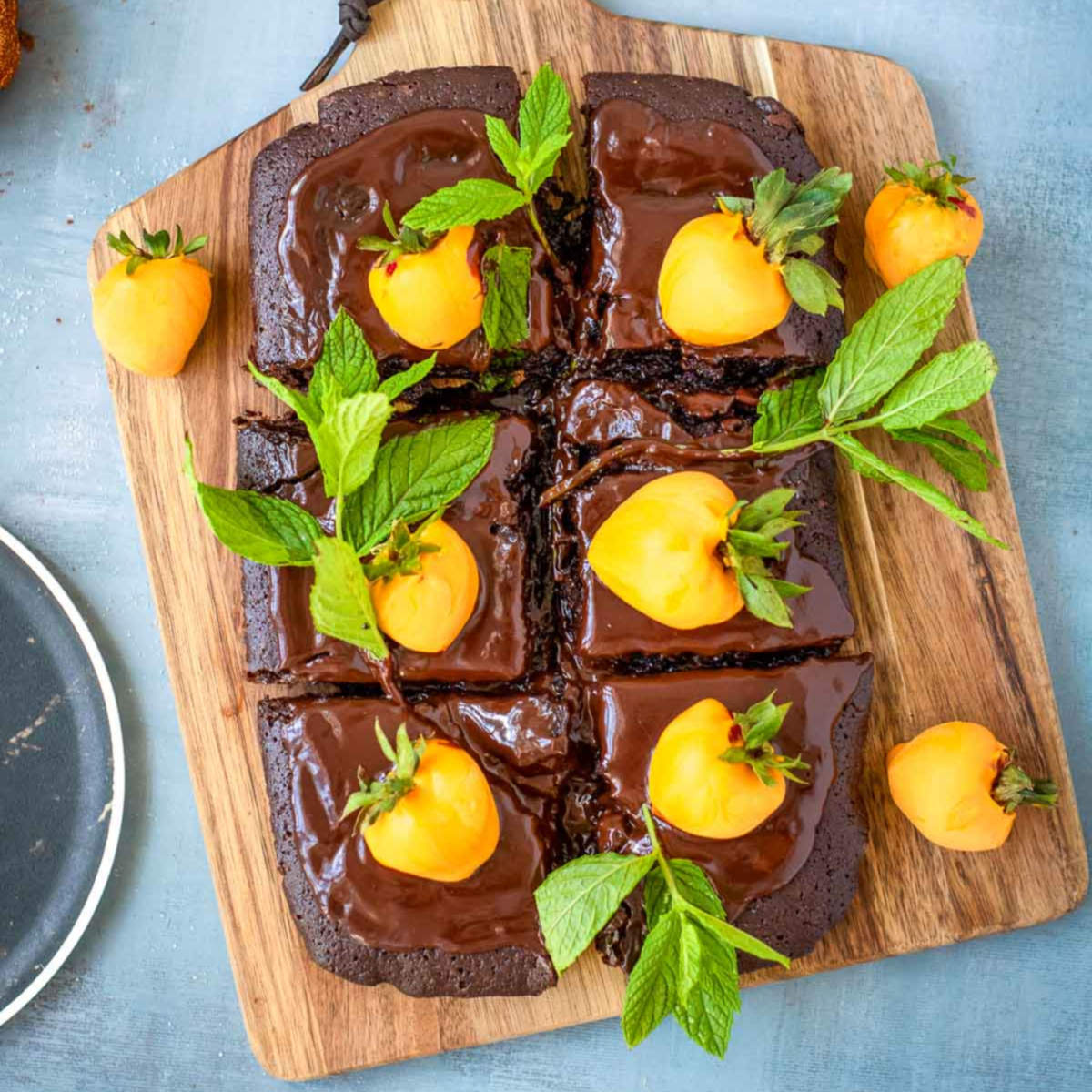 Sliced chocolate brownie cake topped with orange-dipped strawberry pumpkins and fresh mint leaves on a wooden board.