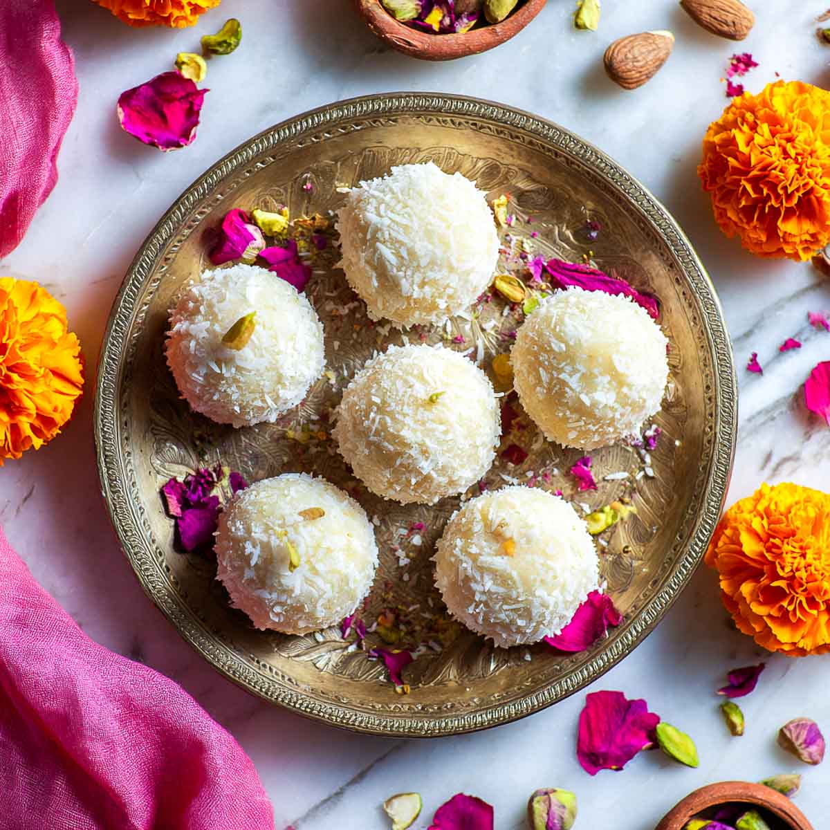 Decorative brass plate with coconut ladoos, rose petals, and marigold flowers.