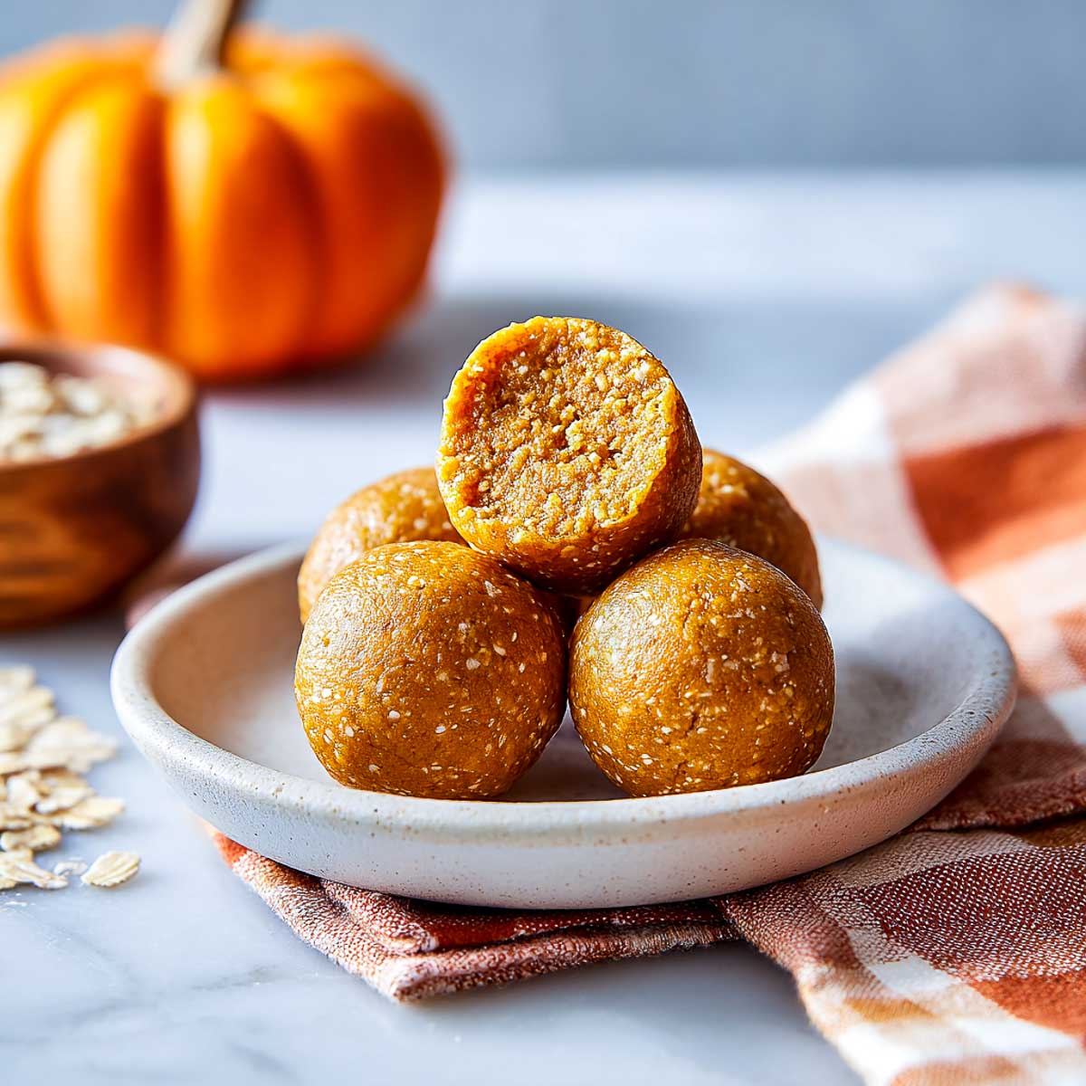 Pumpkin protein bites with a bitten ball on a small white plate.
