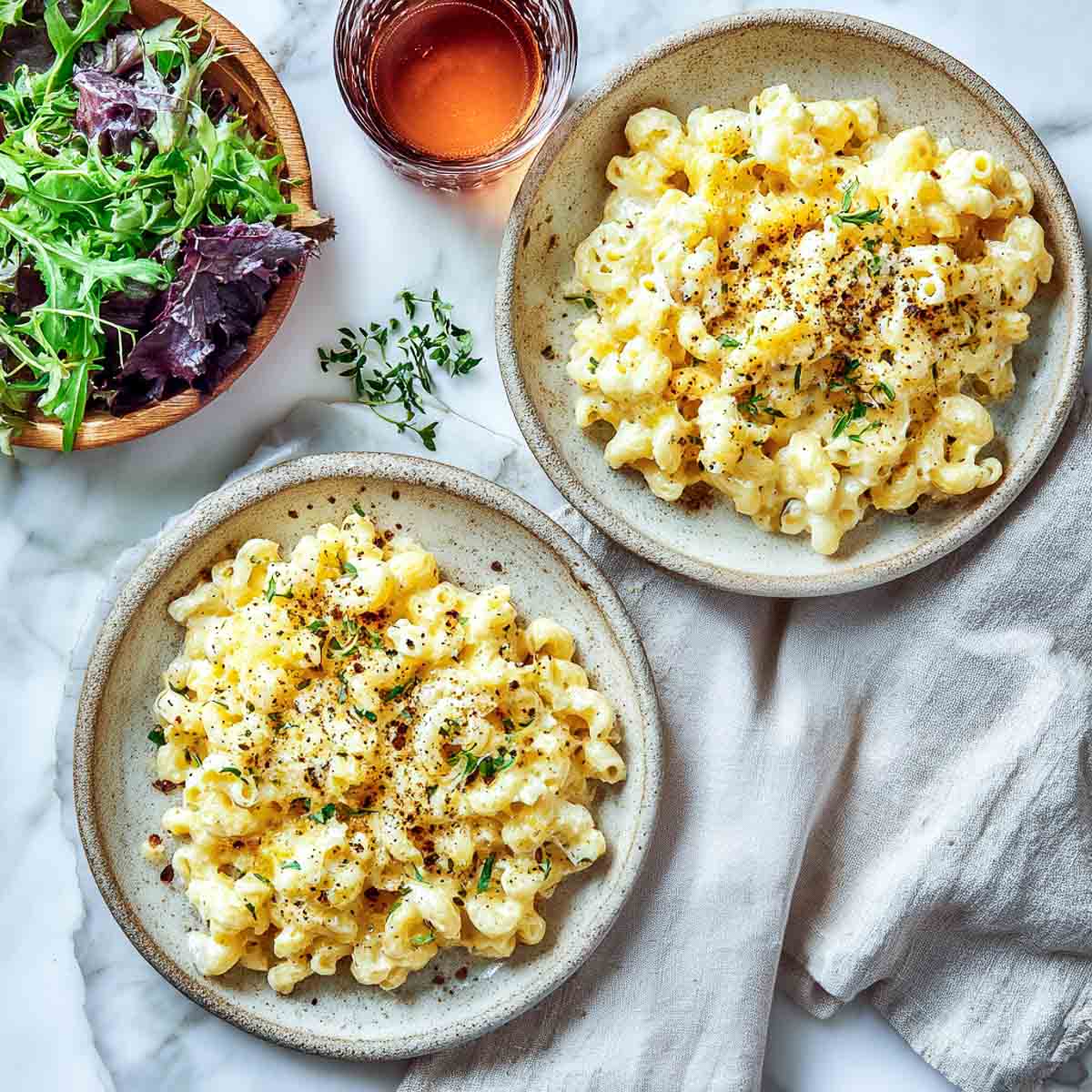 Two plates of cottage cheese mac and cheese served with salad and herbs.
