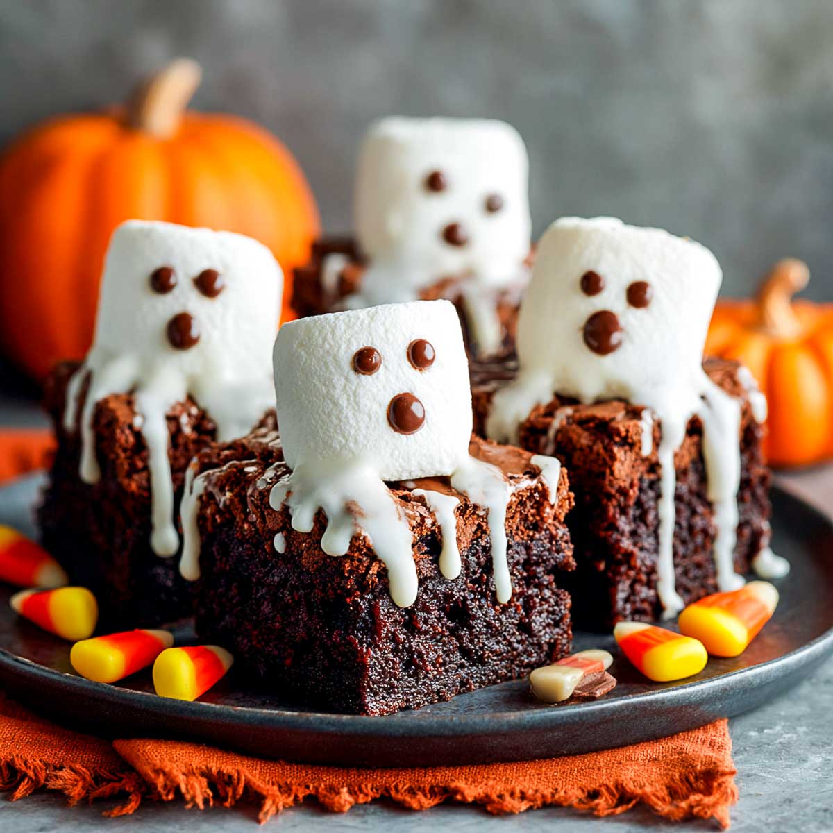 Side view of ghost brownies topped with marshmallow ghosts drizzled in white chocolate.