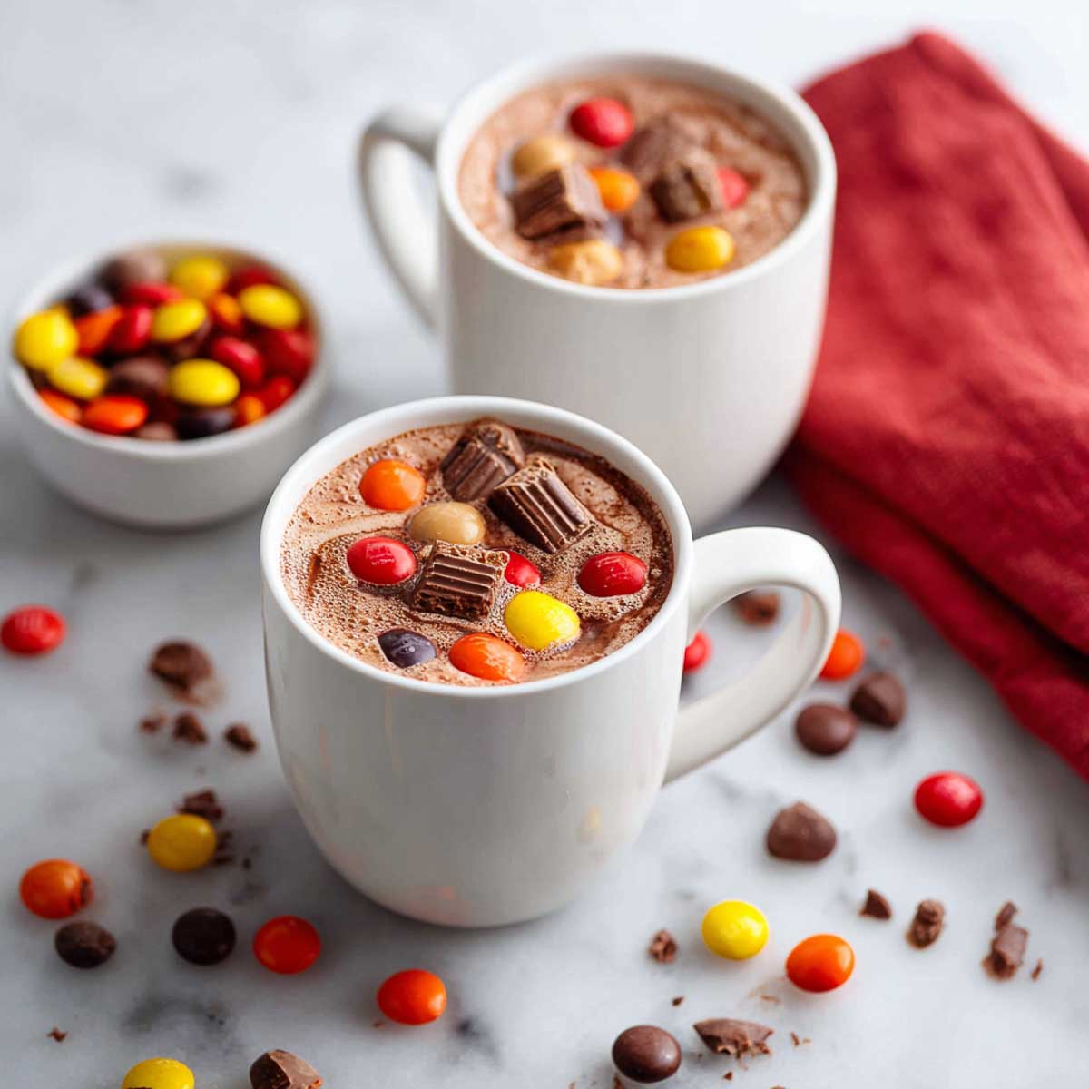 Two mugs of hot chocolate with leftover Halloween candies melting in.
