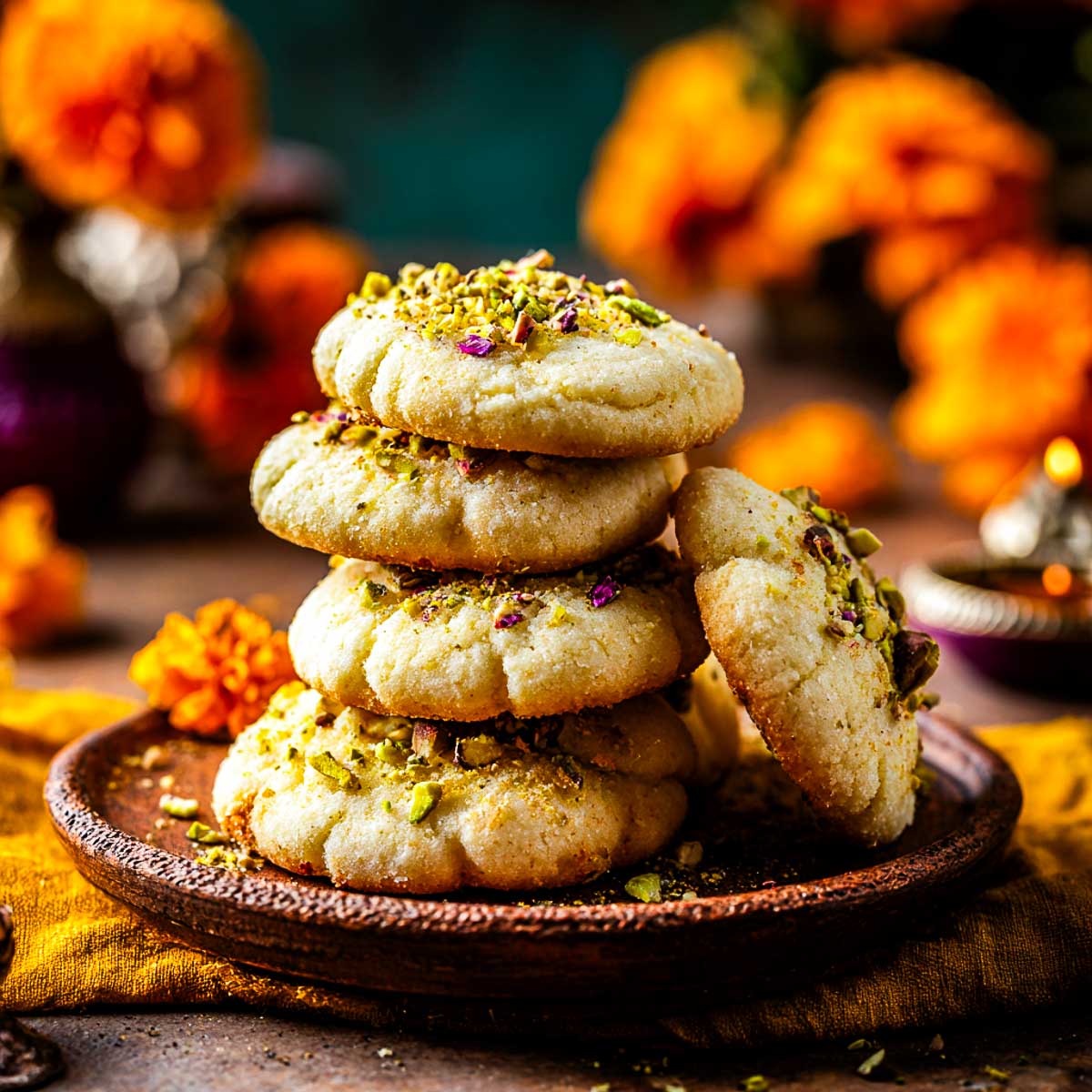 Stack of soft nankhatai cookies topped with pistachios on festive plate.