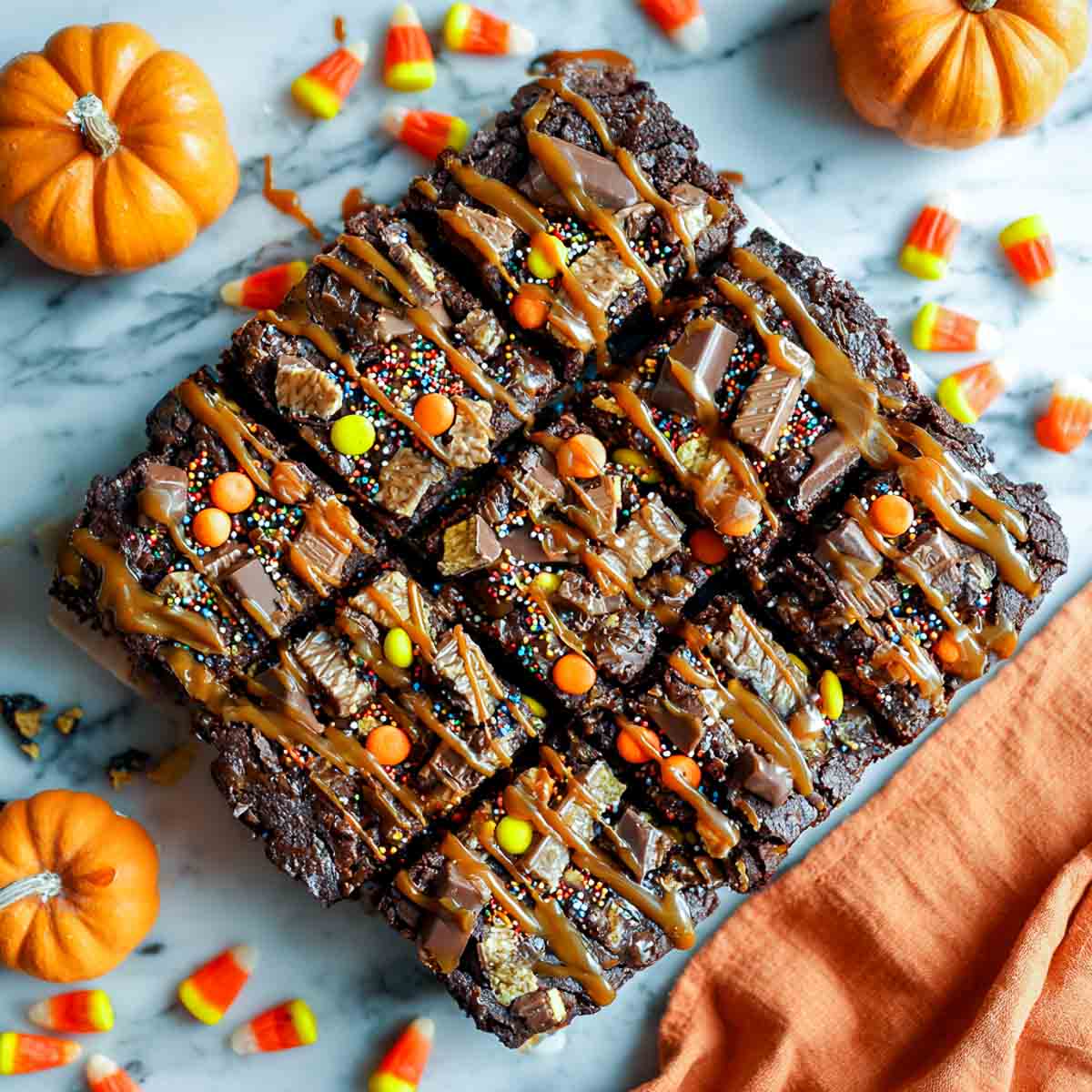 Top-down view of Over-the-Top Halloween brownies cut into squares, topped with assorted candy bars, caramel drizzle, and festive sprinkles.