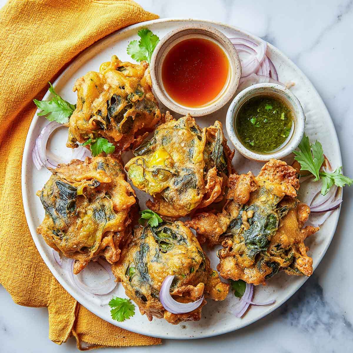 Golden palak pakoras on a plate with green and tamarind chutney.