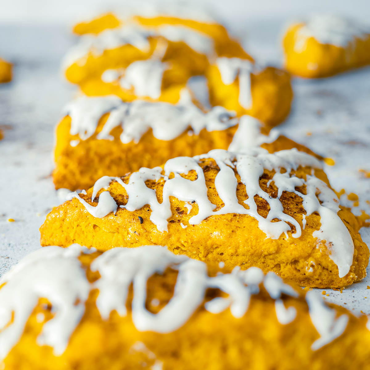Golden pumpkin spice scones in a row with thick vanilla glaze drizzle.