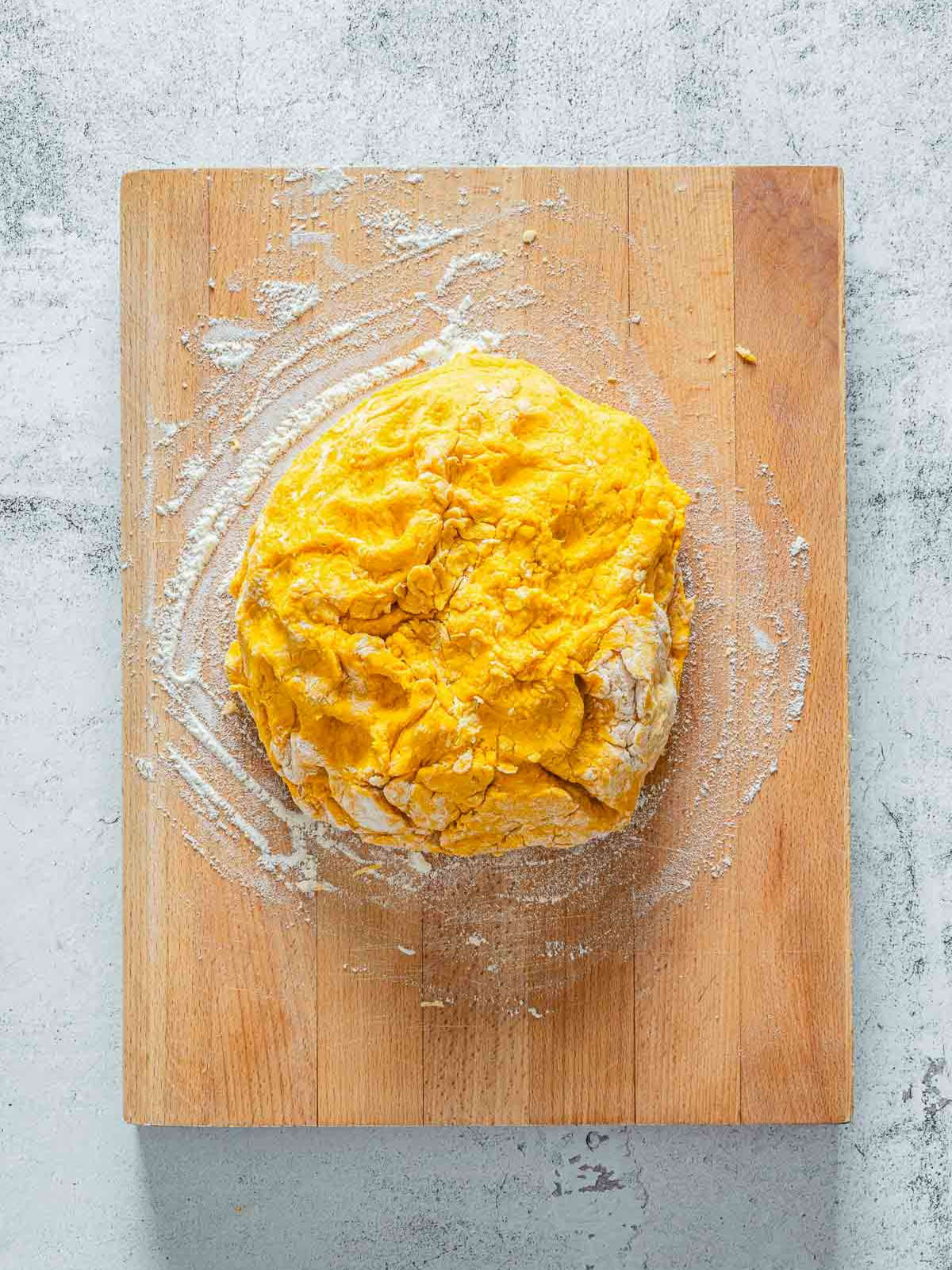 Pumpkin scone dough shaped into a rustic ball on floured wooden board.