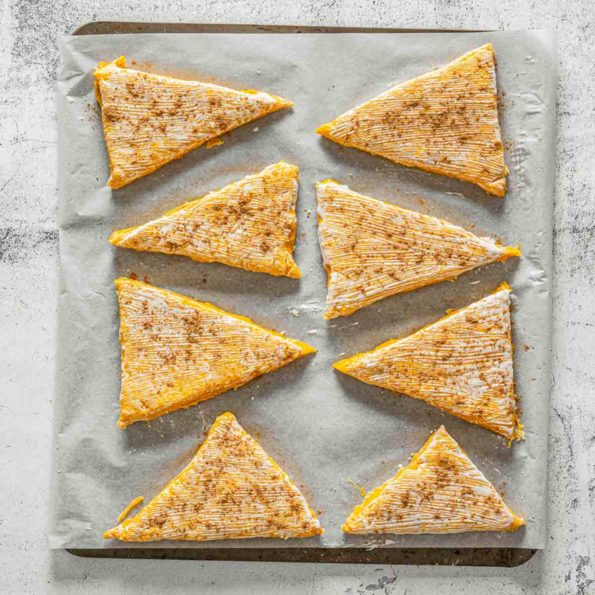 Pumpkin scone wedges brushed with cream and sprinkled with spice before baking.