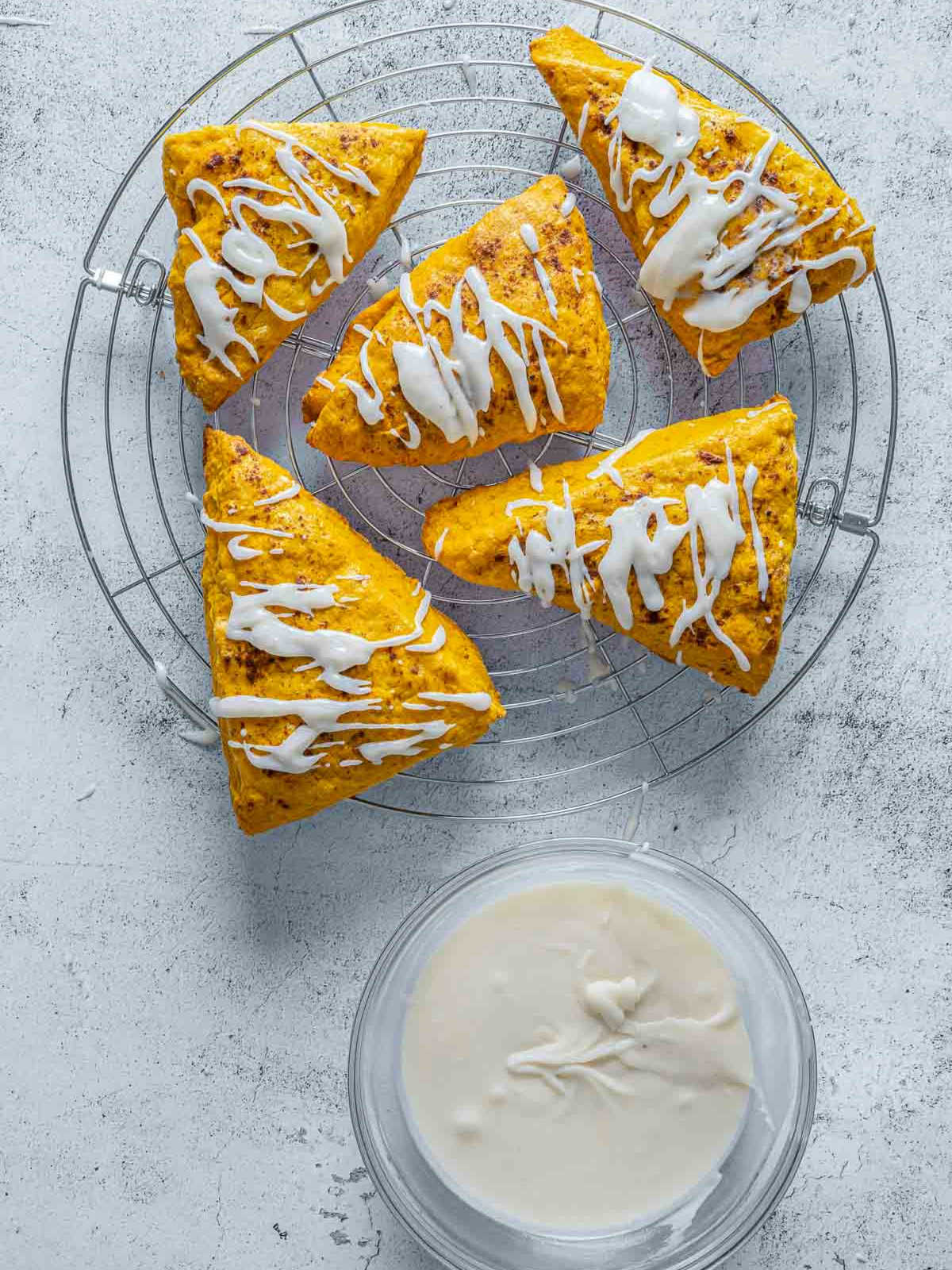 Pumpkin spice scones drizzled with vanilla glaze cooling on wire rack