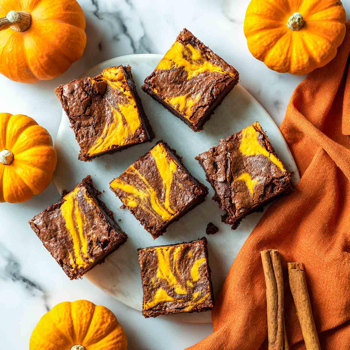 Top-down view of gooey pumpkin swirl brownies with vibrant pumpkin cheesecake swirls, surrounded by mini pumpkins and cinnamon sticks.