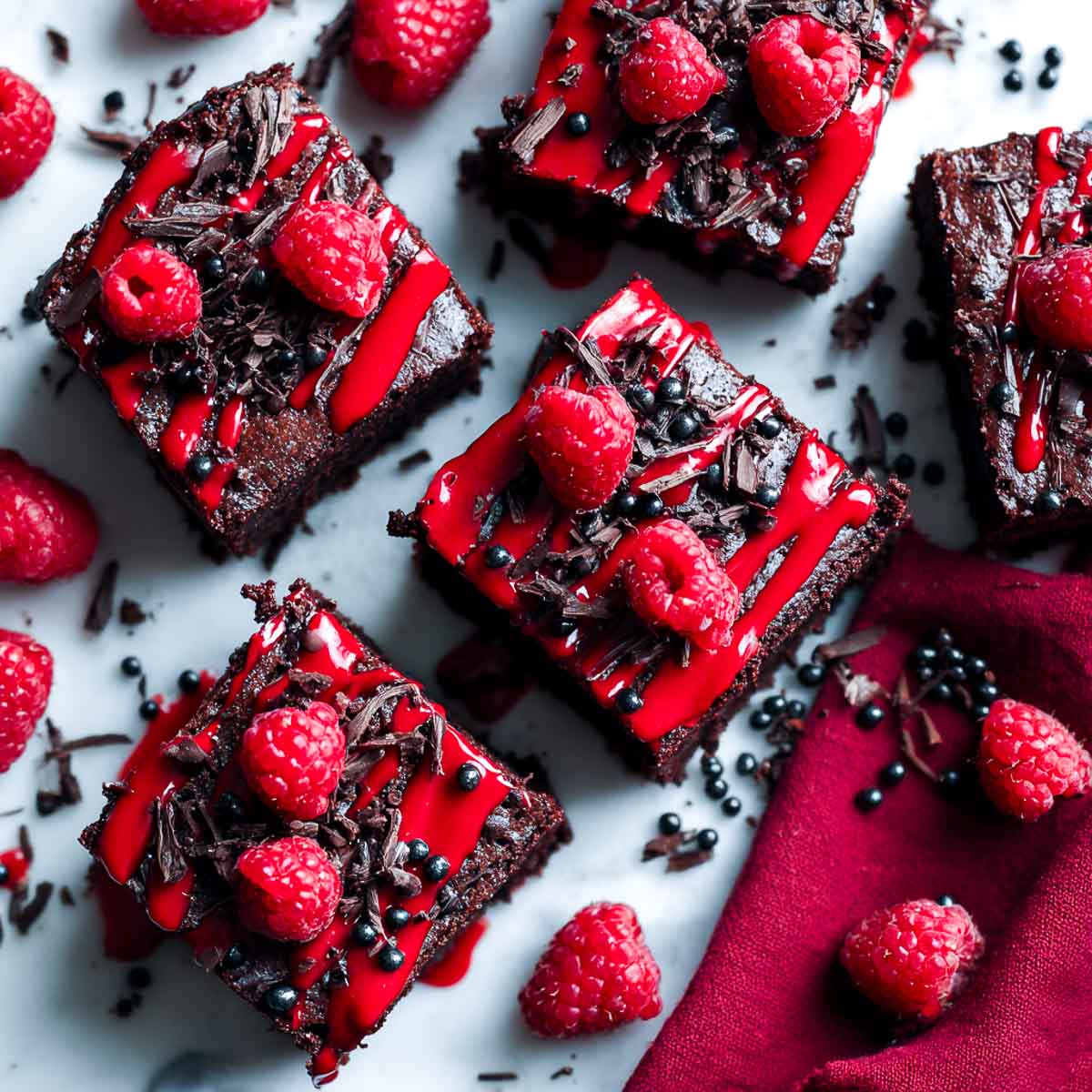 Top-down view of raspberry drizzle brownies with fresh raspberries, chocolate shavings, and red raspberry sauce.