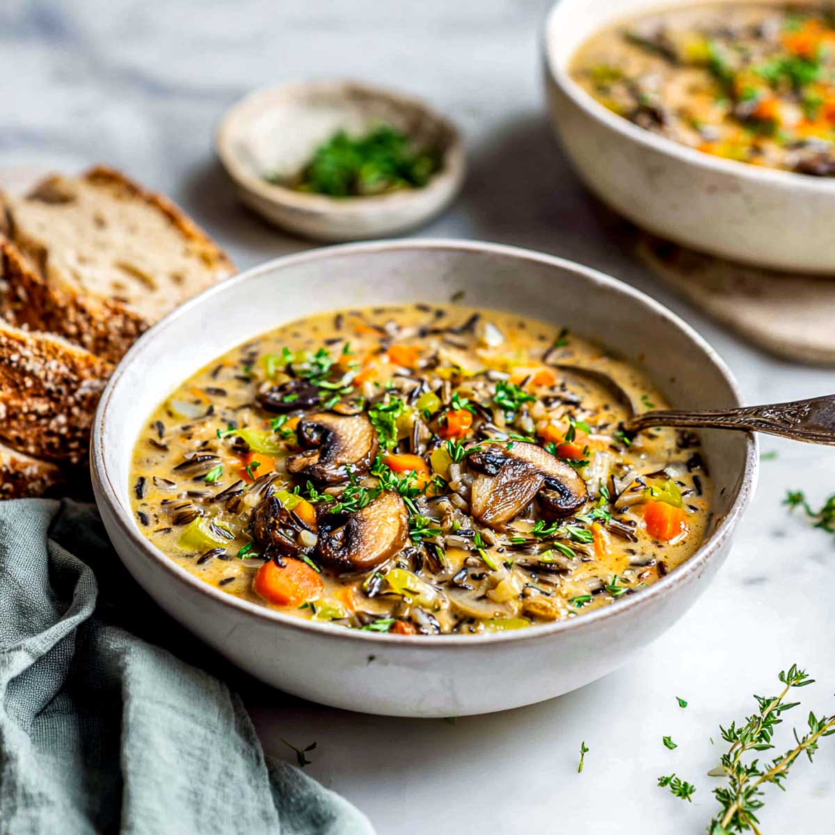 Creamy vegan wild rice and mushroom soup with fresh herbs in white bowl.