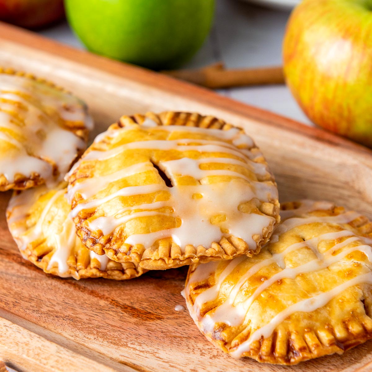 Close-up of glazed apple hand pies on a wooden serving tray with a green apple in the background.