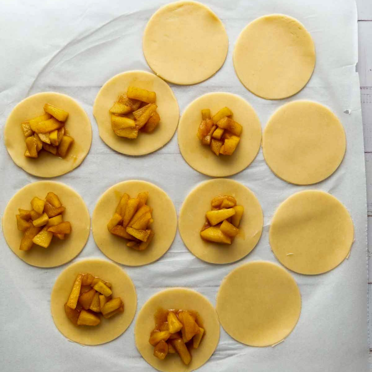Pie dough circles topped with spoonfuls of apple filling, ready to assemble.