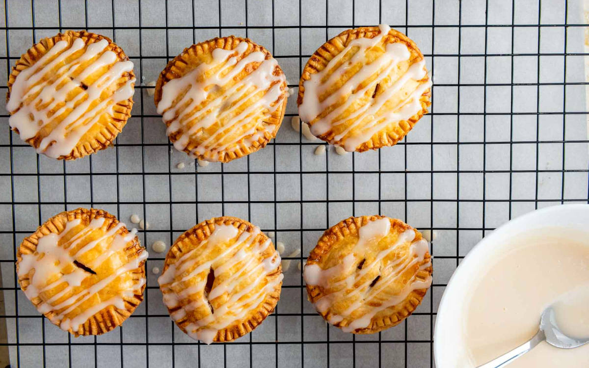 Apple hand pies drizzled with icing cooling on a wire rack.