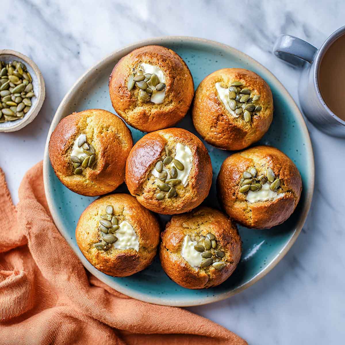 Golden pumpkin muffins with cream cheese centers and pumpkin seeds on plate.