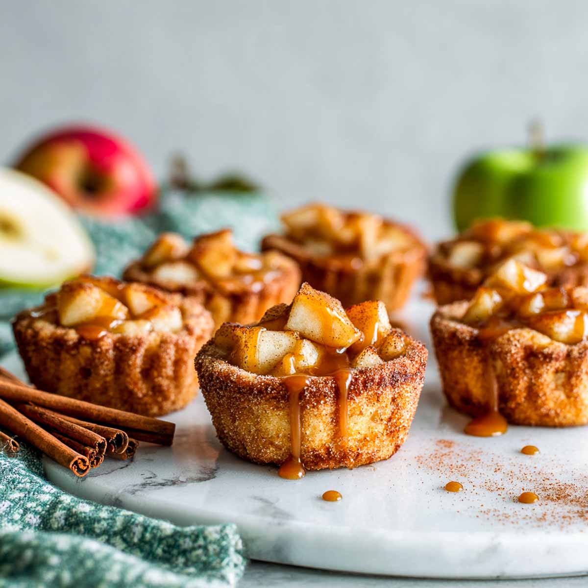 Mini gluten-free churro apple pie cups with golden cinnamon-sugar crusts, apple pie filling, and caramel drizzle.