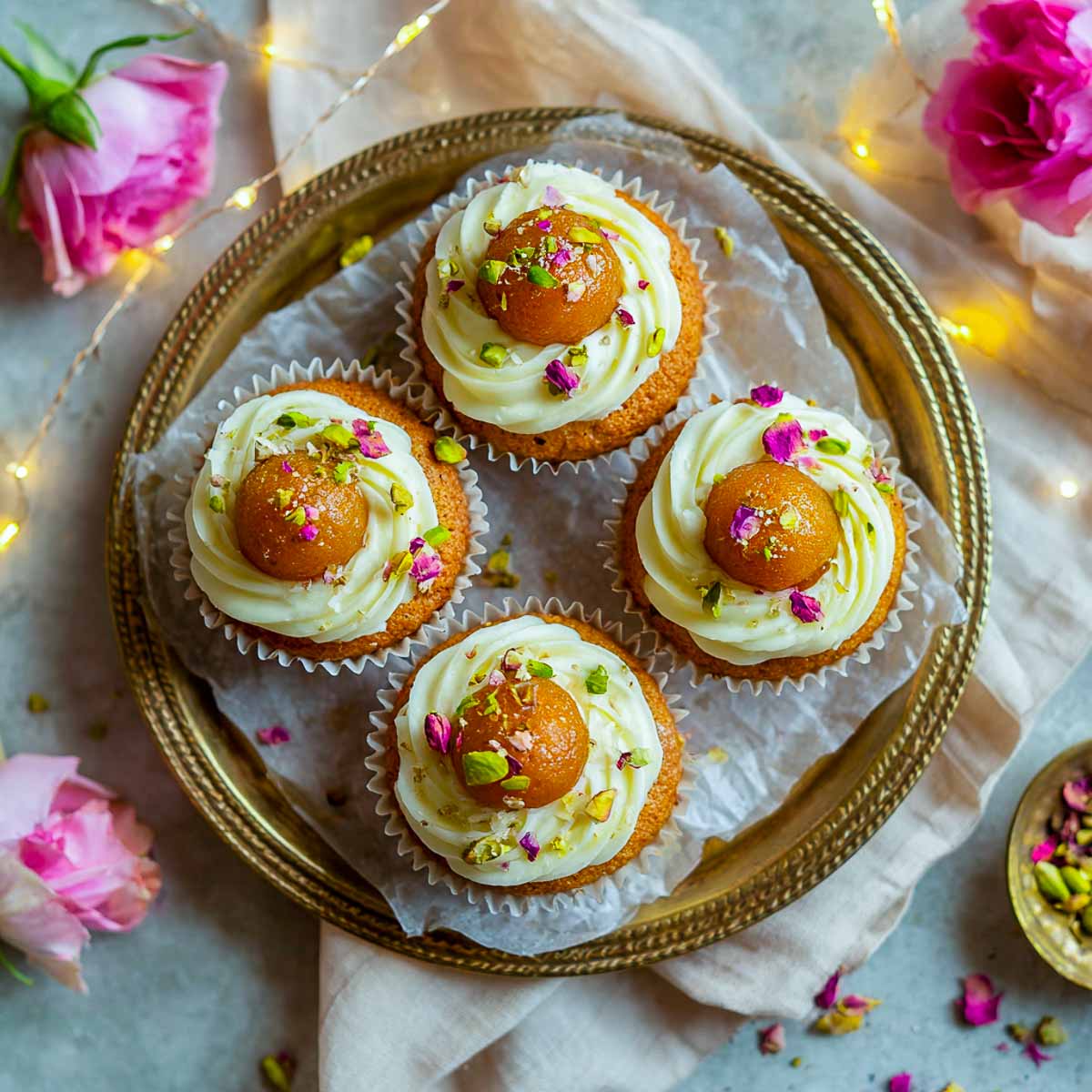 Tray of gulab jamun cupcakes topped with syrup, pistachios, and festive roses.