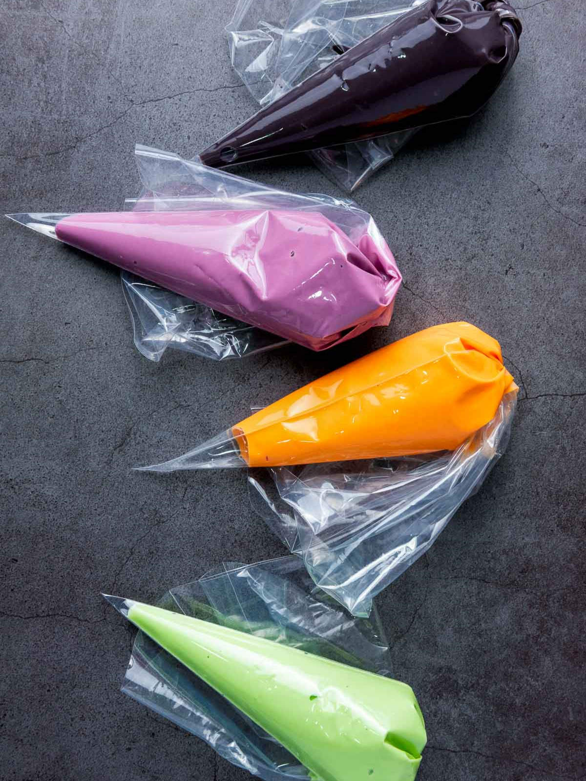 Piping bags filled with melted Halloween candy colors on dark surface.
