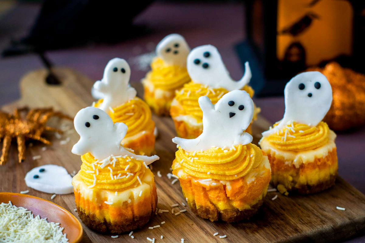 Festive cheesecakes decorated with orange swirls, sprinkles, and ghost toppers.