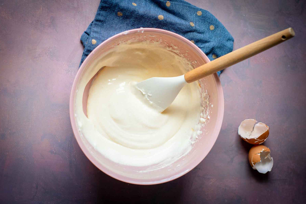 Mixing bowl with creamy cheesecake batter and a spatula on the side.