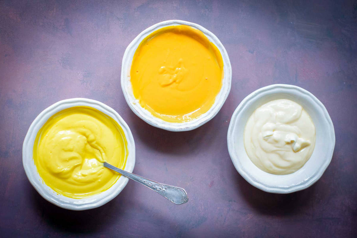 Three bowls of cheesecake batter tinted orange, yellow, and white.