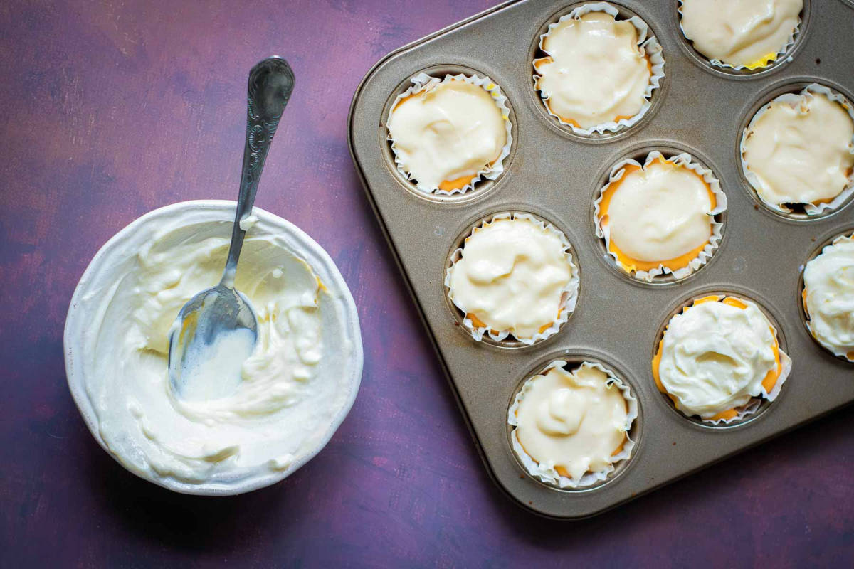 Cupcake pan filled with layered cheesecake batter ready to bake.