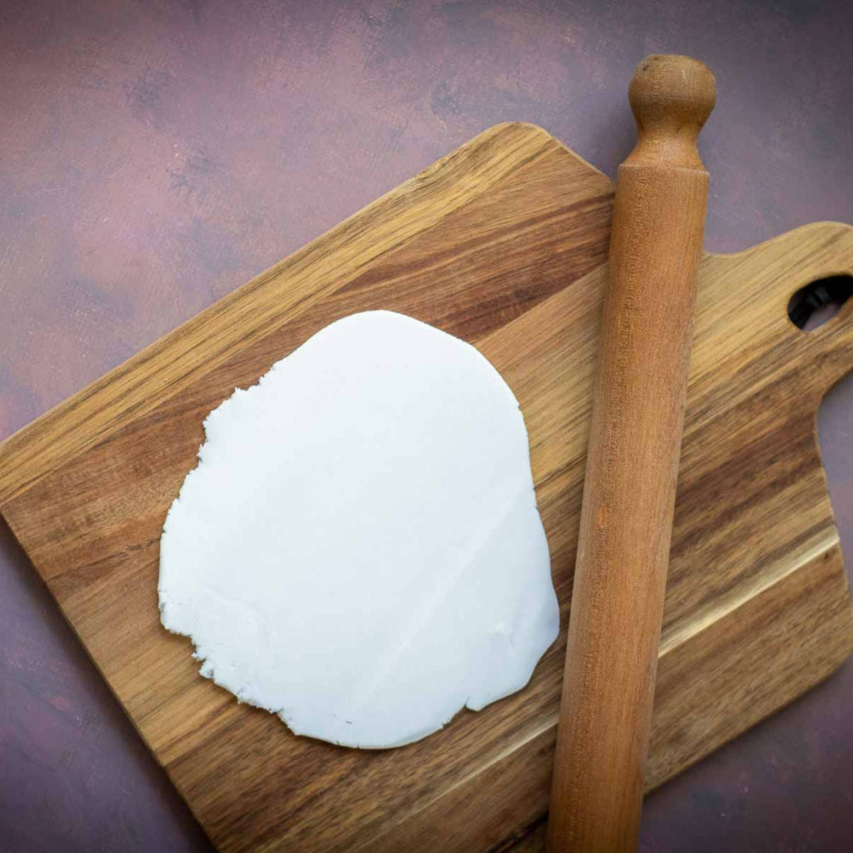 Rolled white fondant on a wooden board with a rolling pin.