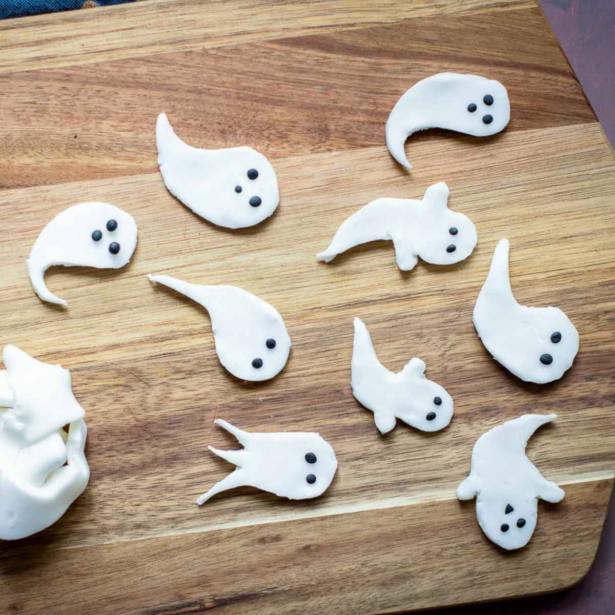 Fondant ghost cutouts with black eyes arranged on a wooden board.