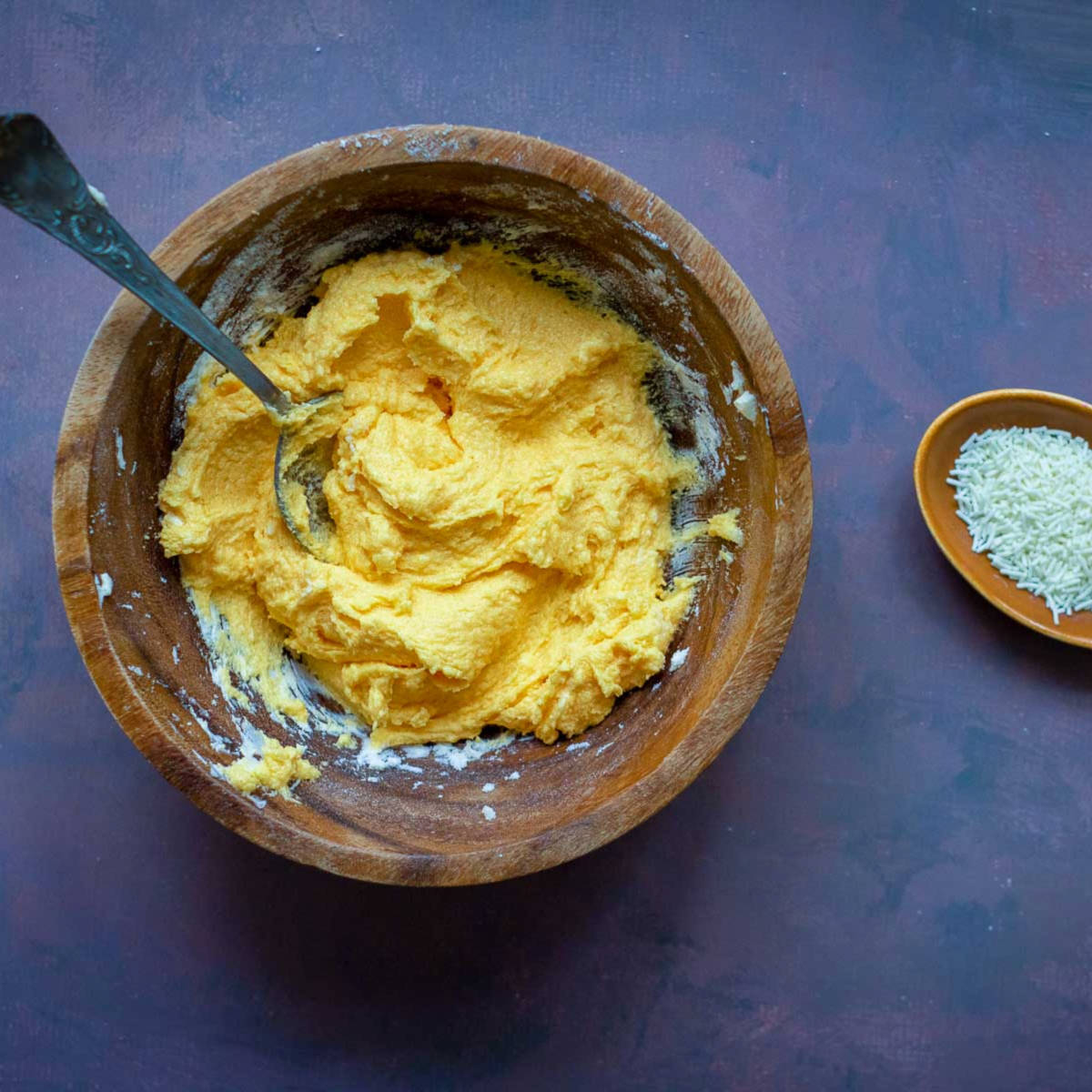 Bright orange cheesecake frosting mixture in a bowl with sprinkles nearby.