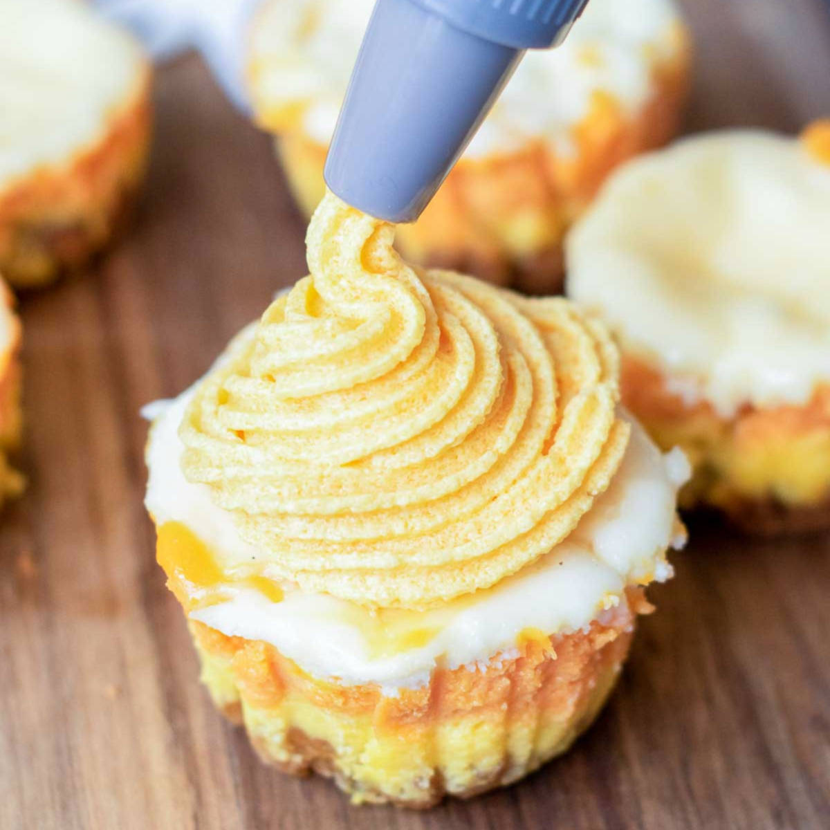 Piping bag decorating mini candy corn cheesecake with orange frosting swirl.